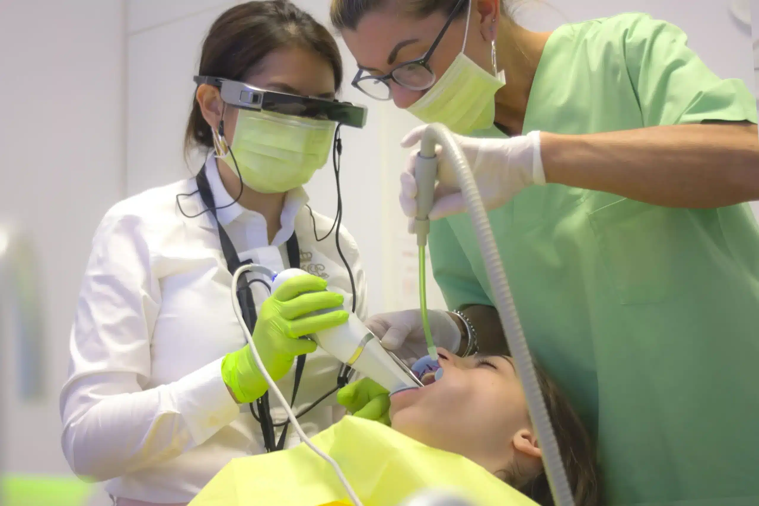 Root Canal Treatment in North Oakville - Two dental professionals in masks and gloves treat a patient lying in a dental chair. One uses a scanning device, while the other assists, all in a modern dental clinic.
